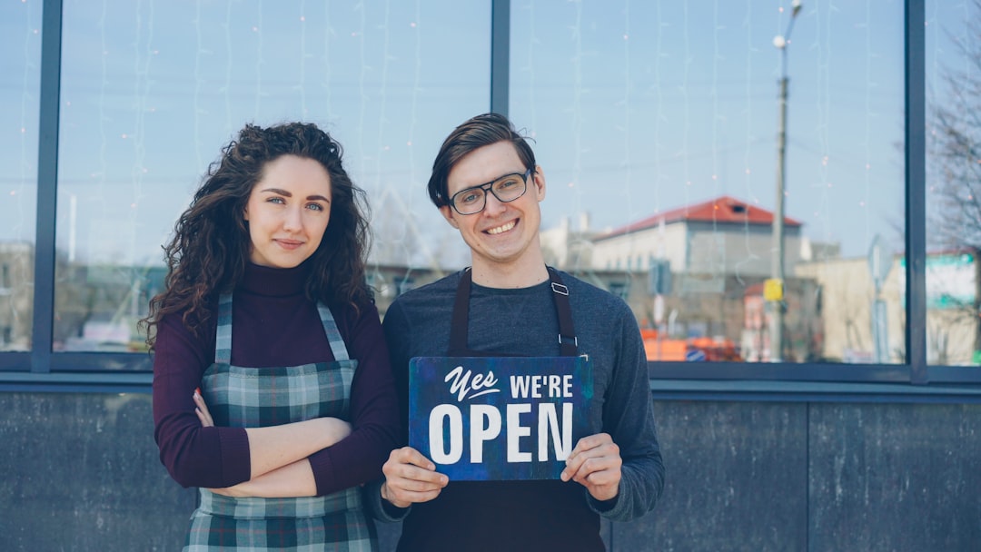 Two people stand outside with an "open" sign.