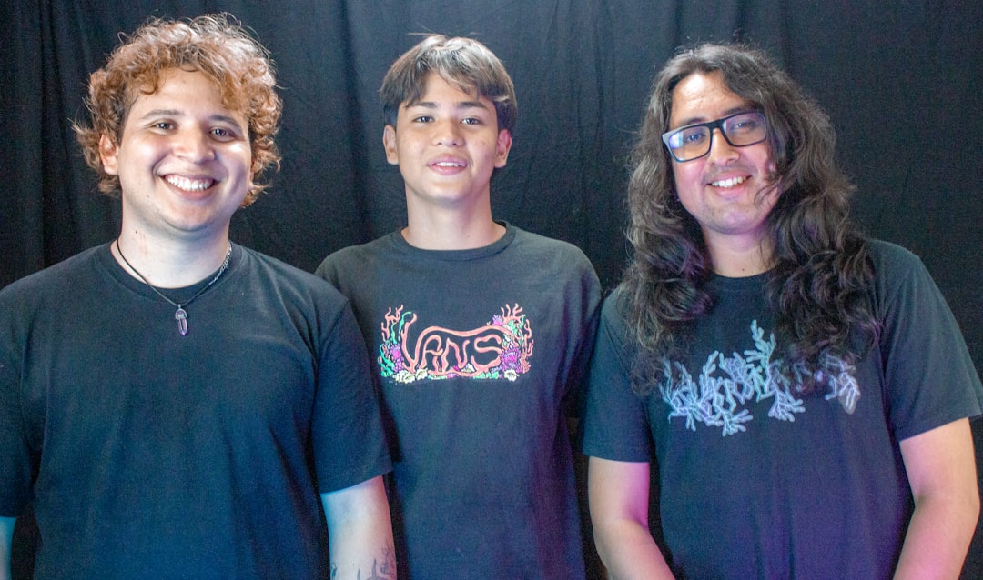 Three smiling young men standing together indoors.